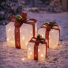 Decorative lighted presents in the snow with a festive background