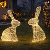 Two illuminated rabbit-shaped outdoor decorations on a grassy lawn with a blurred festive background.